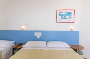 Quarto de hotel com uma cama de solteiro, mesas de cabeceira, um telefone fixado na parede e um quadro emoldurado.