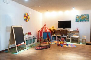 Habitación pensada para niños con una pizarra, una carpa de juegos, un carrusel y un televisor.