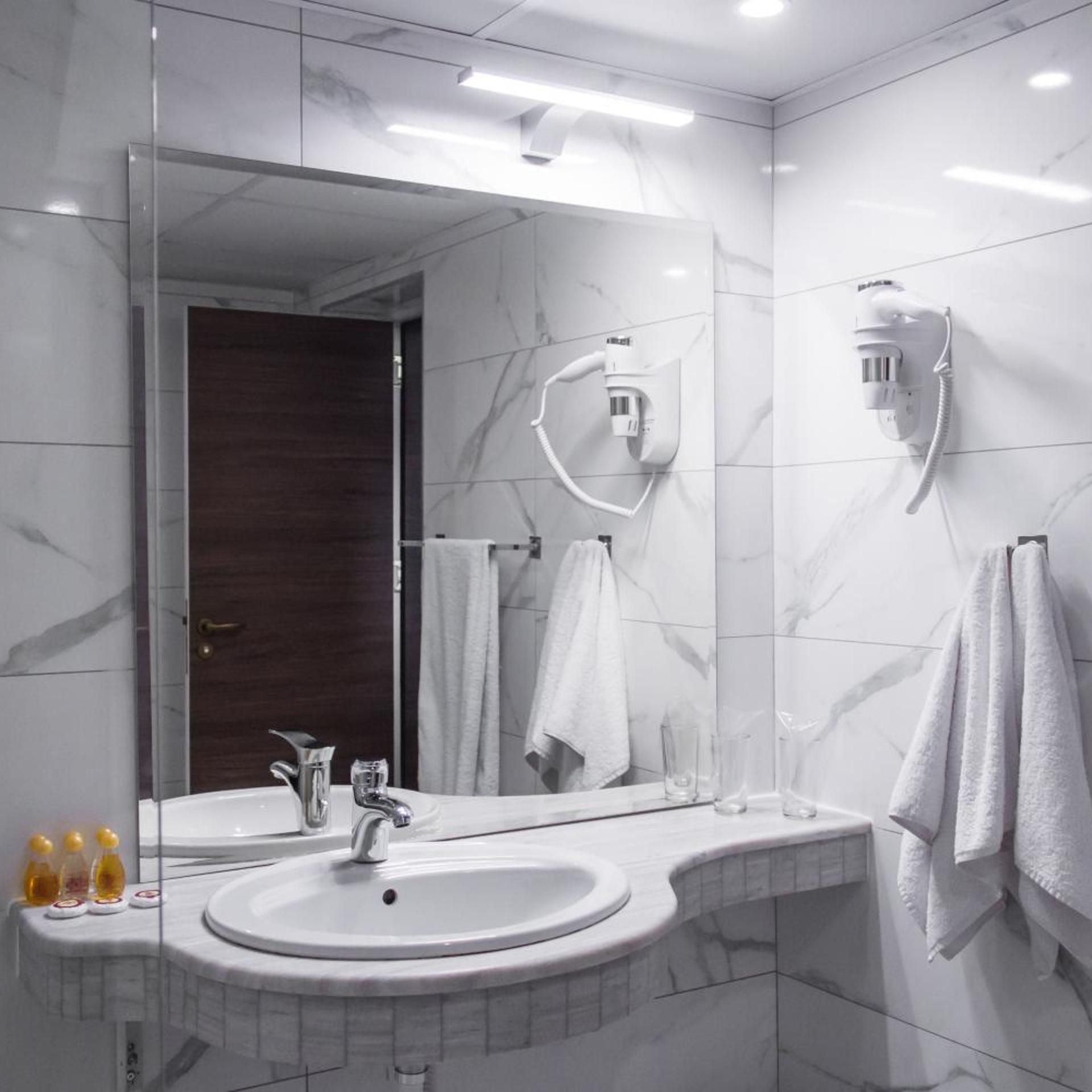 A modern bathroom with a large mirror, a sink, a towel rack, and a hairdryer mounted on the wall.
