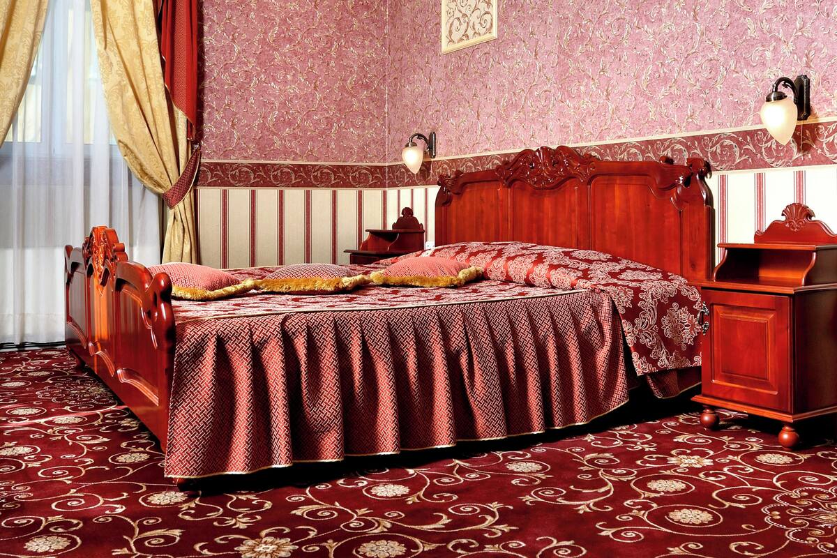 A room with a large bed, a wooden nightstand, a desk, and a chandelier.