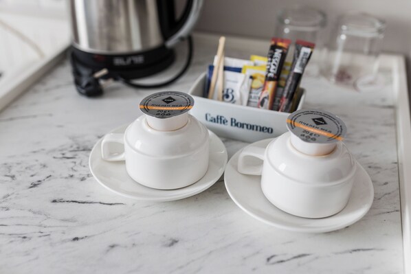 Two white ceramic cups with lids on a marble countertop, a coffee maker, and a box labeled "Caffe Boromeo" in the background. - Anna Palace (Ruse)