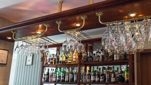 Baarialue, jossa on viiniteline, hyllyt täynnä alkoholijuomapulloja ja tietokonenäyttö.
