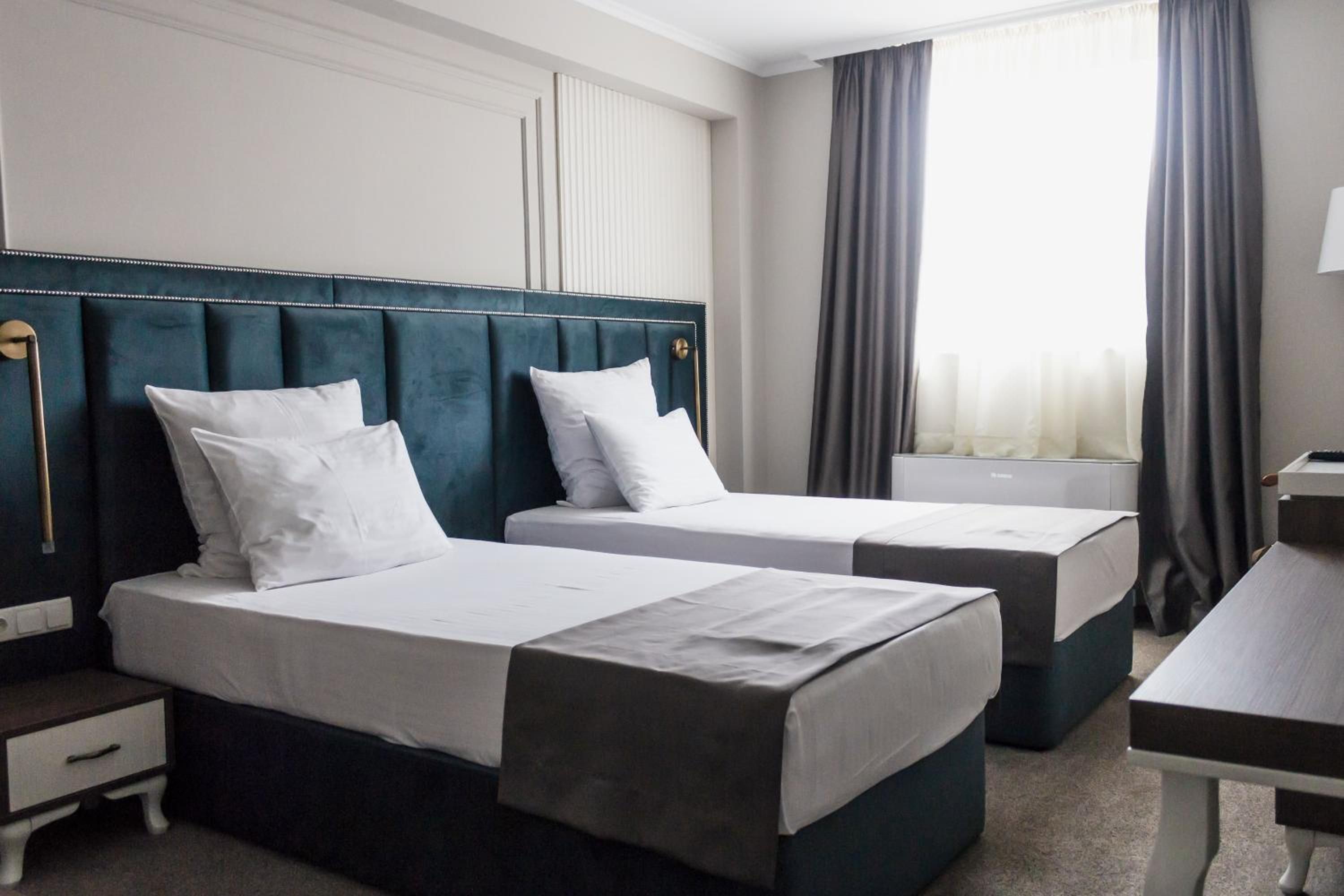 Ein Hotelzimmer mit zwei Betten, einem Schreibtisch und einem Fenster mit Vorhängen.