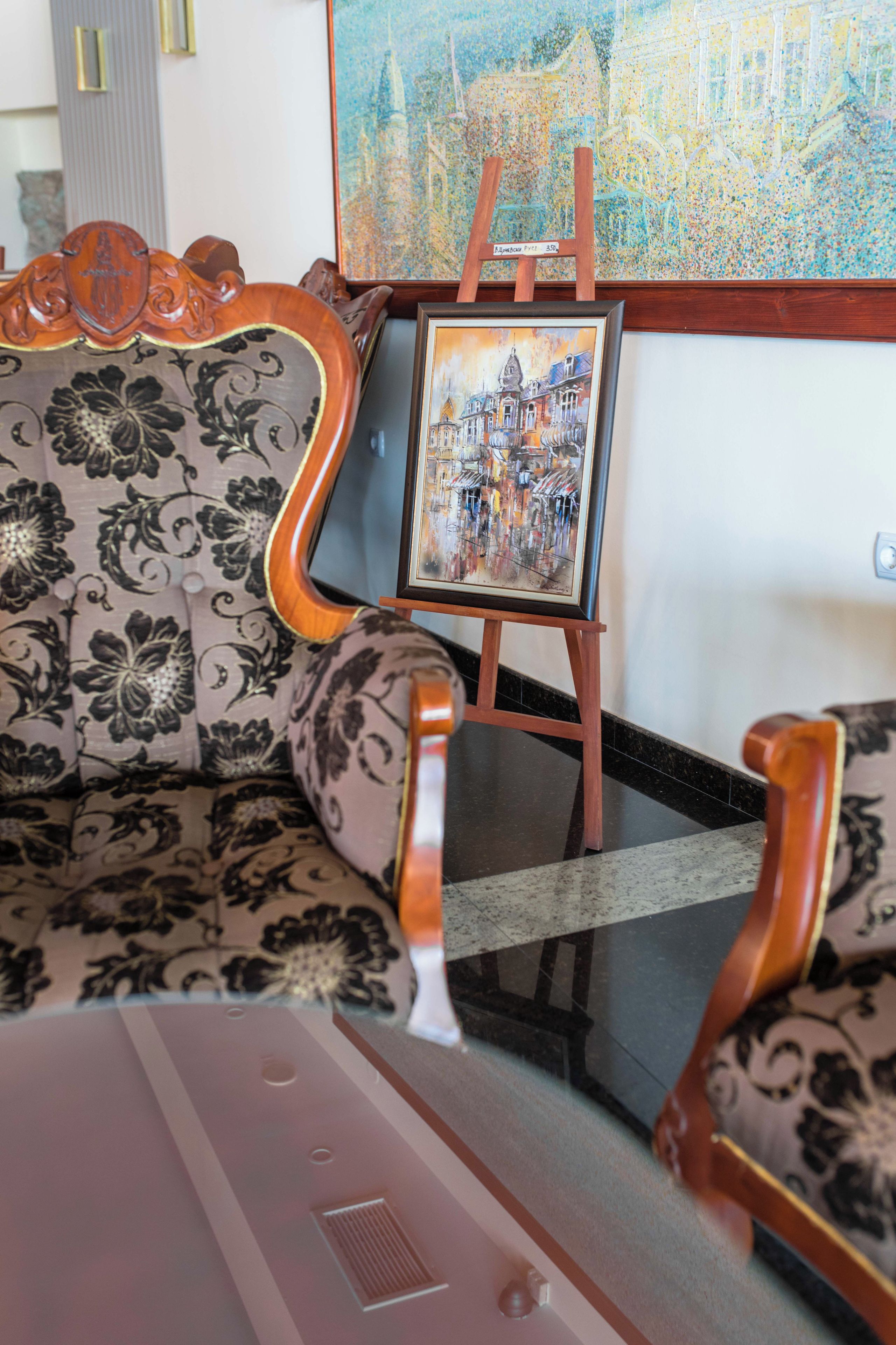Ein Zimmer mit einer gemusterten Couch, einem gerahmten Gemälde auf einem Lehrstuhl und einem Fliesenboden.