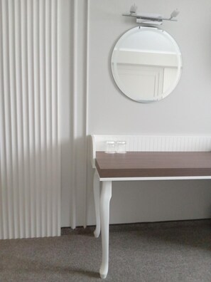 A room with a white radiator, a round mirror on the wall, and a wooden table with two glasses on it.