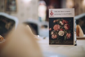 A card with a floral painting and text in a foreign language, placed on a table. - Anna Palace (Ruse)