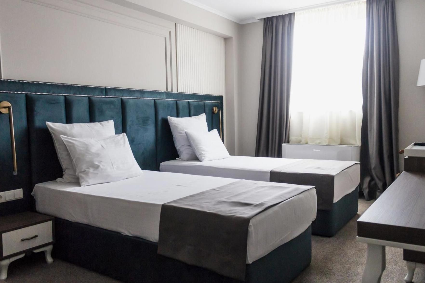 A hotel room with two single beds, a nightstand, a desk, and a window with curtains.