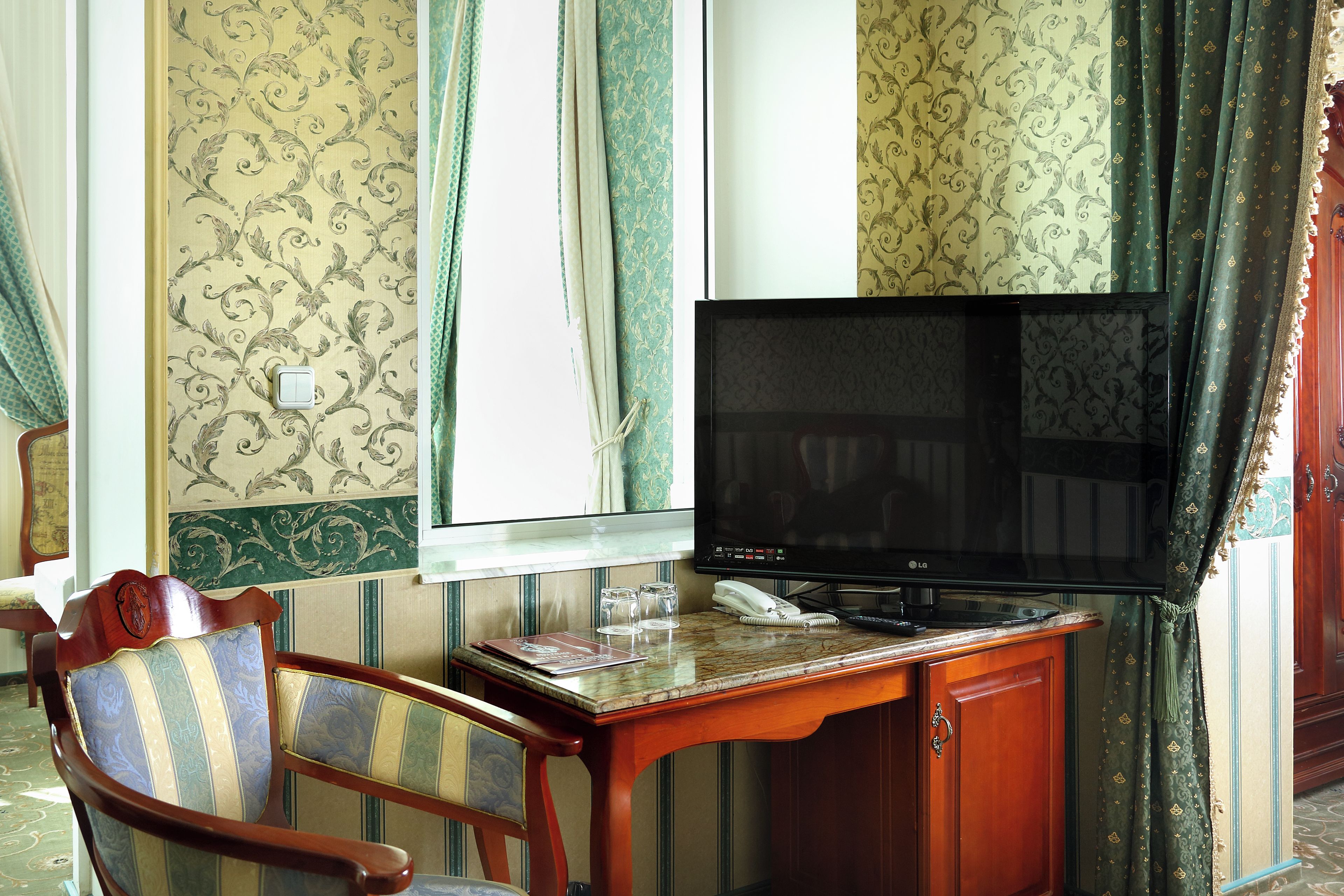 A room with a television on a wooden table, a chair, and patterned wallpaper.