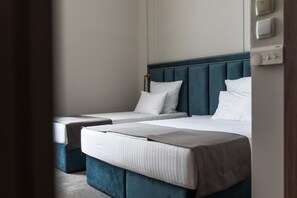 Une chambre d’hôtel avec deux lits, une tête de lit sombre et un thermostat visible sur le mur.