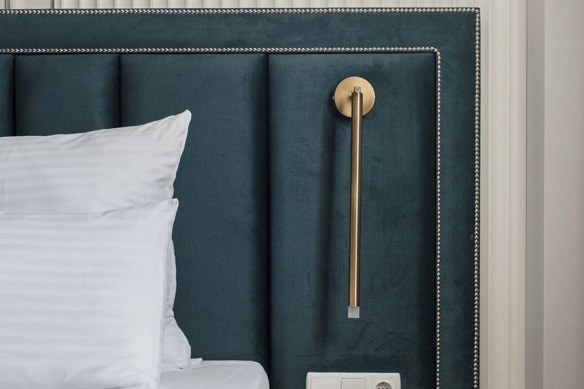 A neatly made bed with white linens, a teal upholstered headboard, and a bedside table with a drawer.