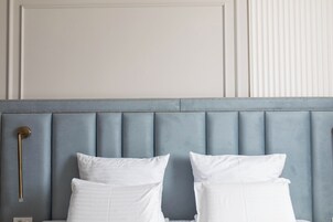 Una cama con cabecera, dos almohadas blancas y una mesita de noche con una lámpara.