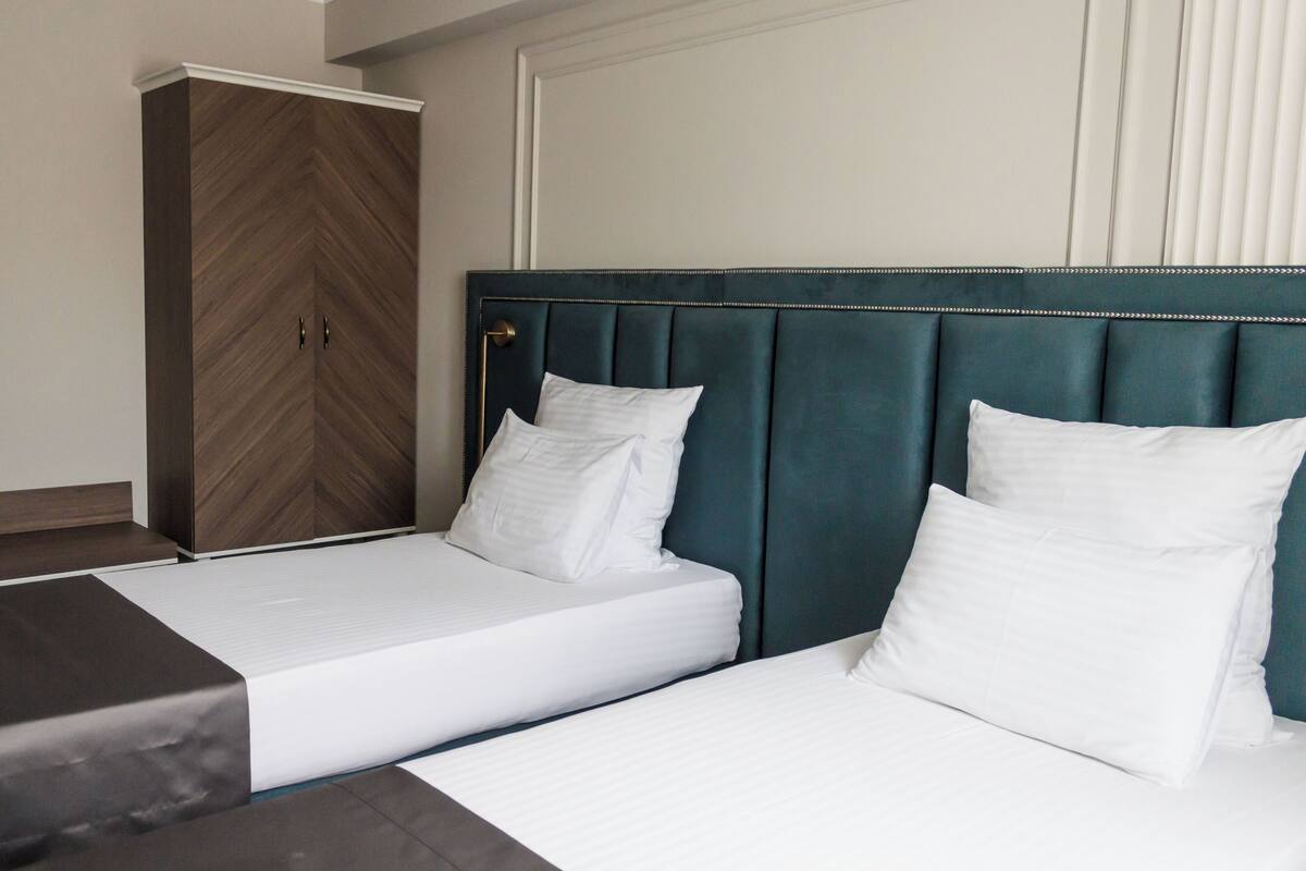 A hotel room with two beds, a wardrobe, and a large window with blinds.