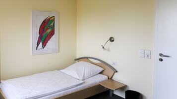 Een enkel bed met houten frame en een wit matras in een kamer met een lichtgele muur.