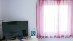 Ein Zimmer mit einem Flachbildfernseher, einer Fernbedienung, einer Wasserflasche und einer Schachtel auf einem Holztisch.