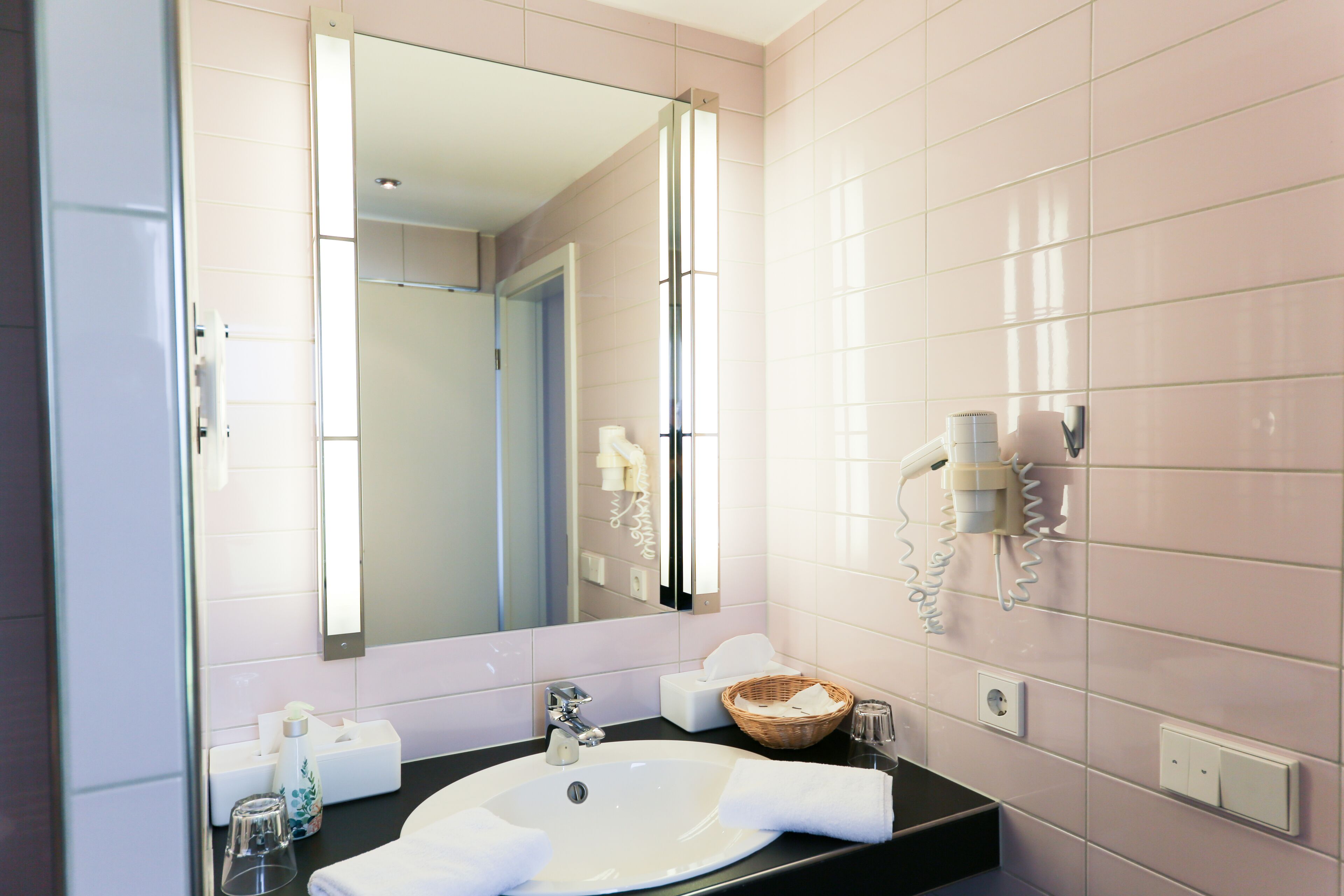 Ein Badezimmer mit Waschbecken, Spiegel, Handtuch, Korb und Fön an der Wand.
