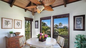 A dining area with a round table, two chairs, a ceiling fan, and framed botanical prints on the walls.