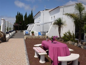 Un edificio blanco con un paseo empedrado, mesas al aire libre y plantas en macetas.