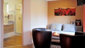 Una sala de estar moderna con un sofá, dos sillones, una mesa de centro con fruta y un cuadro de flores rojas en la pared.