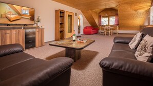 Una habitación estilo loft acogedora, con techo de madera, un televisor de pantalla plana grande, un sofá, una silla roja y un comedor con mesa y sillas.