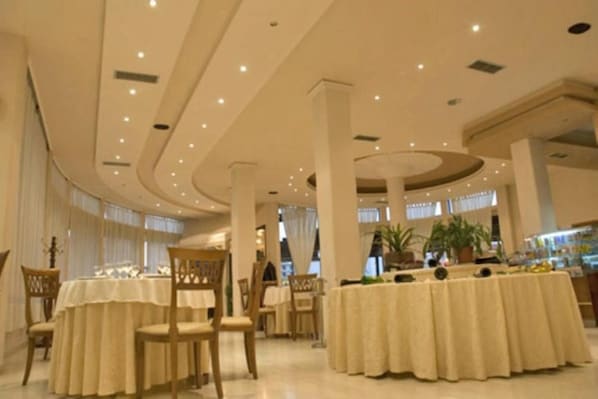 A spacious hotel lobby with multiple round tables, high ceilings, and large windows allowing natural light.