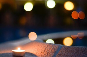 A candle on a textured surface with blurred lights in the background. - Akropoli Hotel (Golem)