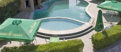 A swimming pool with a curved edge, surrounded by green umbrellas and neatly trimmed hedges.