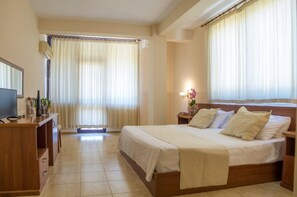 A hotel room with a bed, bedside table, TV, and curtains. - Akropoli Hotel (Golem)
