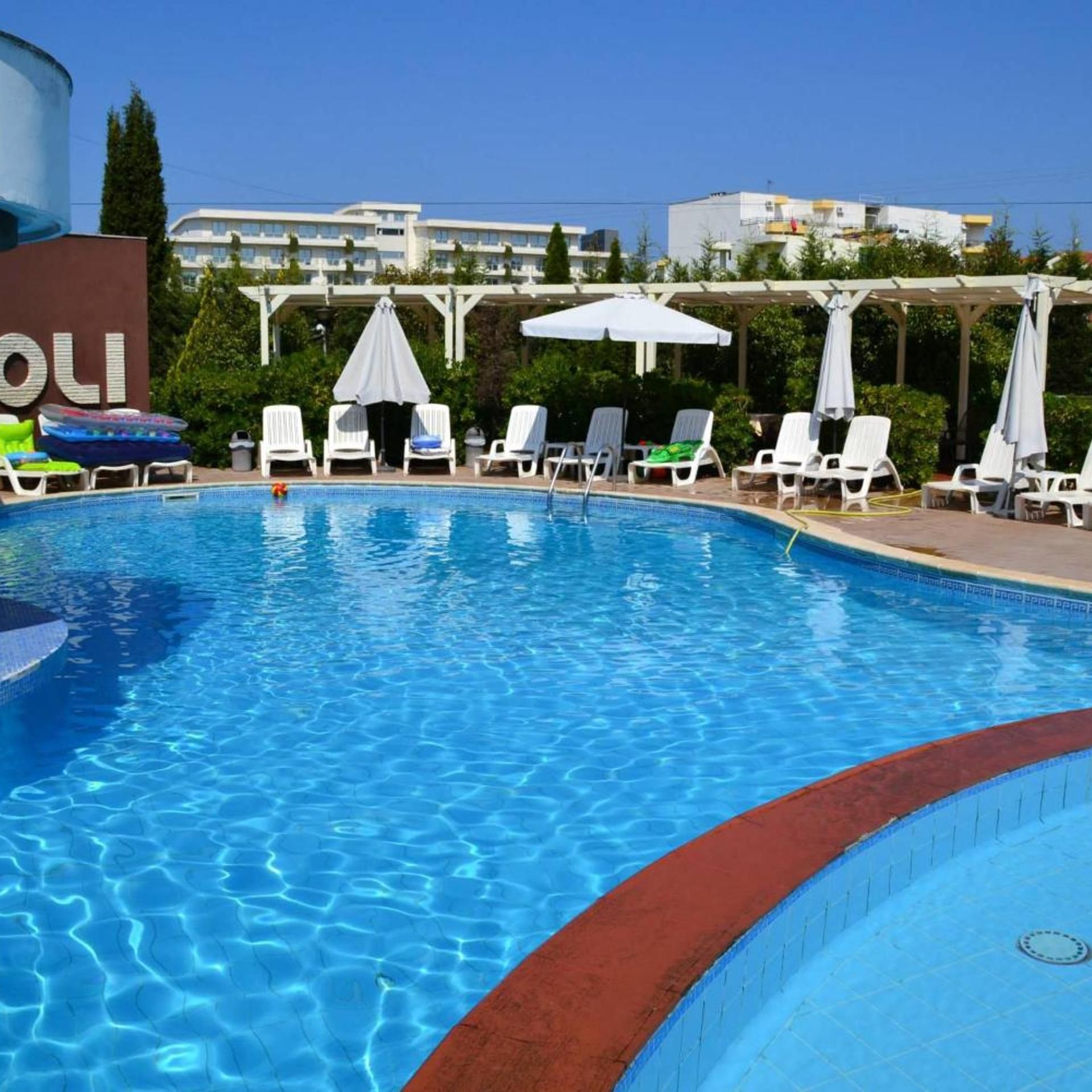 A swimming pool with lounge chairs and umbrellas, surrounded by greenery and buildings.