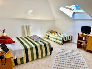 A small, well-lit room with a sloped ceiling, two beds with striped bedding, a desk with a television, and a skylight. - Hotel Villa Ada (Borgio Verezzi)