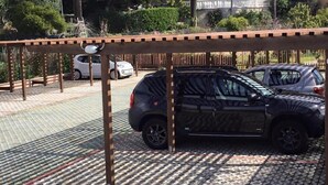 A parking area with a covered section, a white car, and a black car parked. - Hotel Villa Ada (Borgio Verezzi)