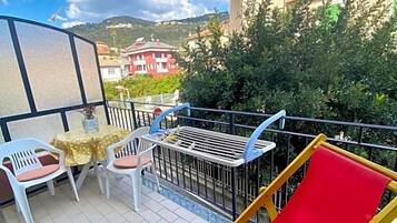 Un balcone con una sedia rossa, un tavolo e sedie, e vista su edifici e alberi.