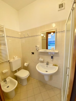 A bathroom with a toilet, bidet, sink, and a mirror with a view of the sea. - Hotel Villa Ada (Borgio Verezzi)