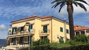 A two-story yellow building with balconies, a palm tree, and a clear sky. - Hotel Villa Ada (Borgio Verezzi)