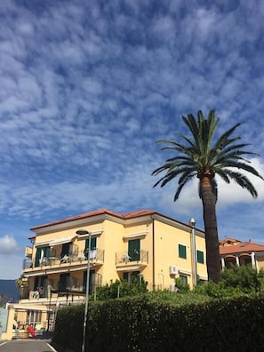 A two-story yellow building with balconies, a palm tree, and a clear sky.
