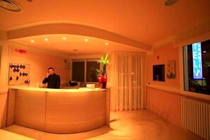 Un'area reception con una scrivania a forma di arco, una pianta in vaso e una finestra con tende.