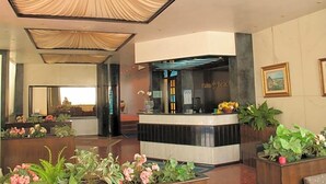 Zona de recepción de hotel con mostrador, plantas y un amplio ventanal.