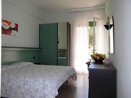 Um quarto com cama, guarda-roupa, escrivaninha com luminária e janela com cortinas.