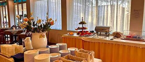 A buffet setup with plates, bowls, and a fruit display.