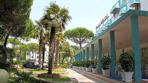 Un hotel con zona de estar al aire libre cubierta, palmeras y un camino de piedra.
