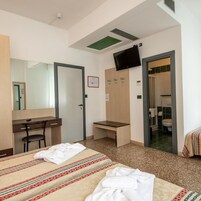 A hotel room with a bed, a desk, a chair, a television, and a bathroom visible through an open door.