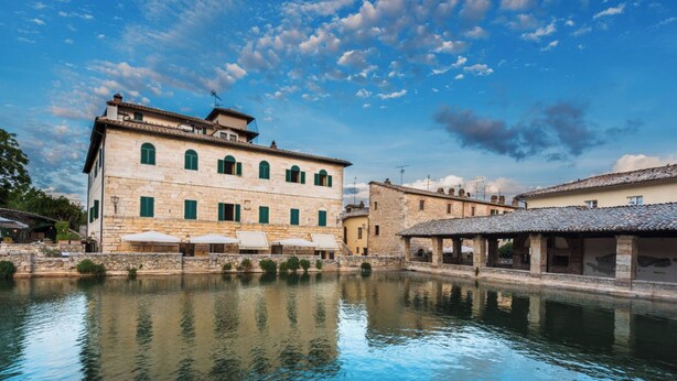 A stone building with a courtyard and a reflective water body. - Palazzo Brandano (Trequanda)