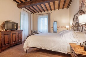 A bedroom with a bed, wooden dresser, and a television on the dresser. - Palazzo Brandano (Trequanda)