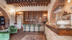 A cozy bar area with a wooden bookshelf, green bar stools, and a rustic brick wall. - Palazzo Brandano (Trequanda)