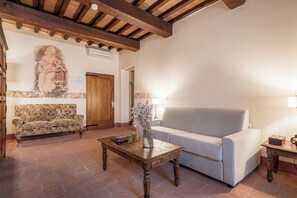 A living room with a wooden coffee table, a floral sofa, a grey sofa, and a stone wall with a fresco. - Palazzo Brandano (Trequanda)