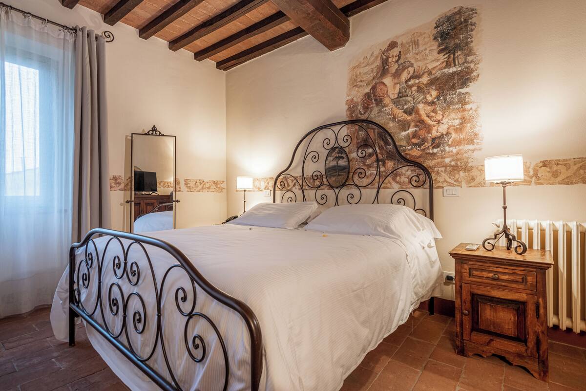 A bedroom with a bed, a nightstand, a mirror, and a radiator.