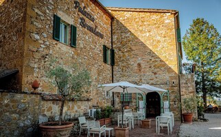 Un edificio de piedra con un letrero que dice "Palazzo Brandino". Hay mesas y sillas al aire libre, plantas en macetas y un gran paraguas.