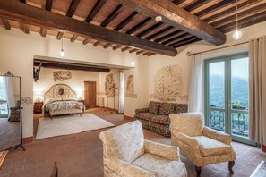 Une pièce spacieuse avec un grand lit, deux fauteuils, un canapé et une vue sur l’extérieur grâce à une grande fenêtre.