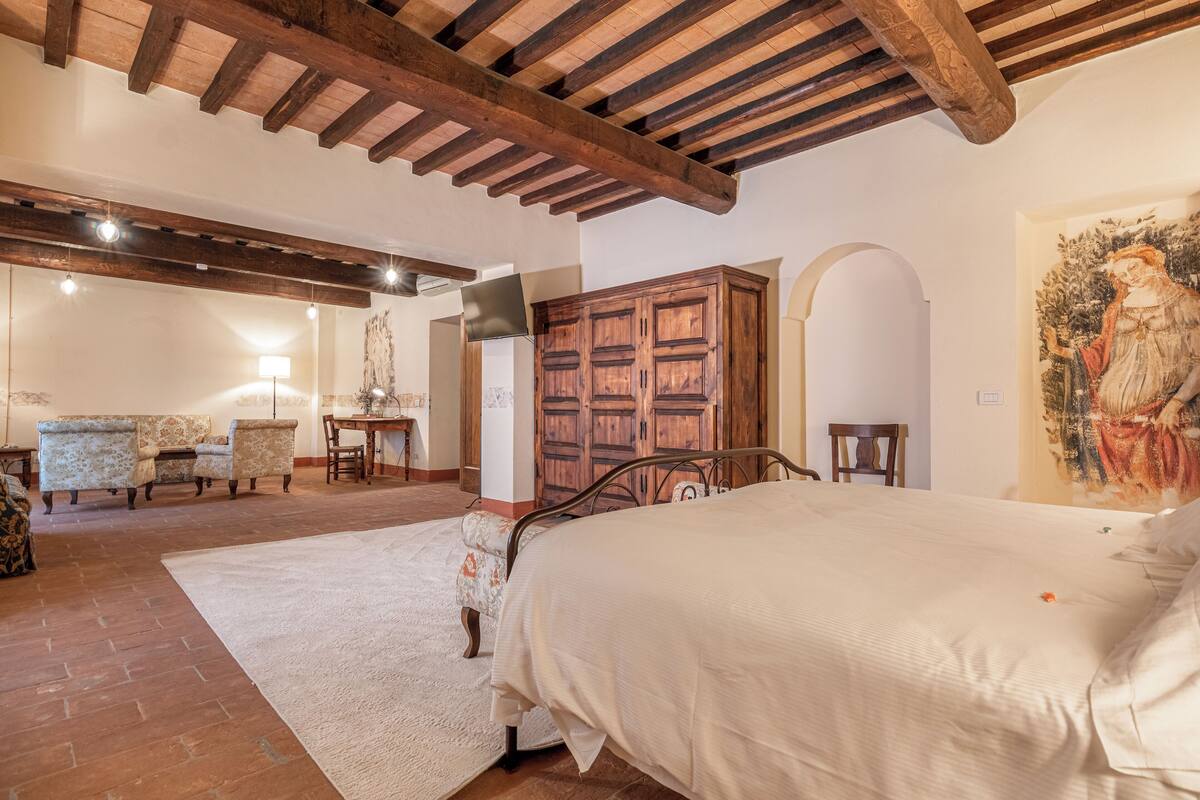 A bedroom with a large bed, wooden wardrobe, and a painting on the wall.
