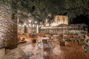 An outdoor patio with brick flooring, wooden tables and chairs, and potted plants. - Palazzo Brandano (Trequanda)
