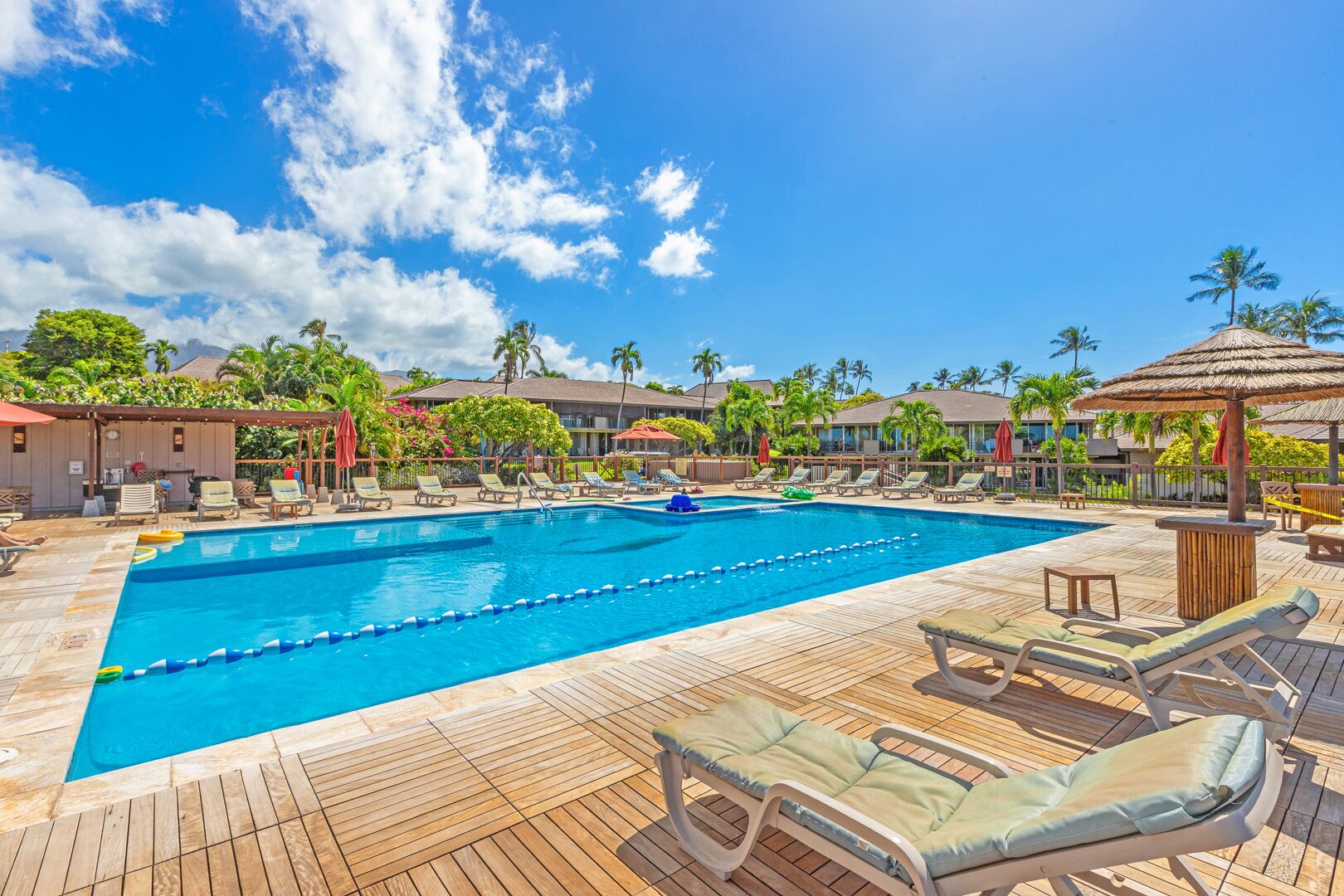 A pool area with lounge chairs and umbrellas, surrounded by palm trees and buildings.